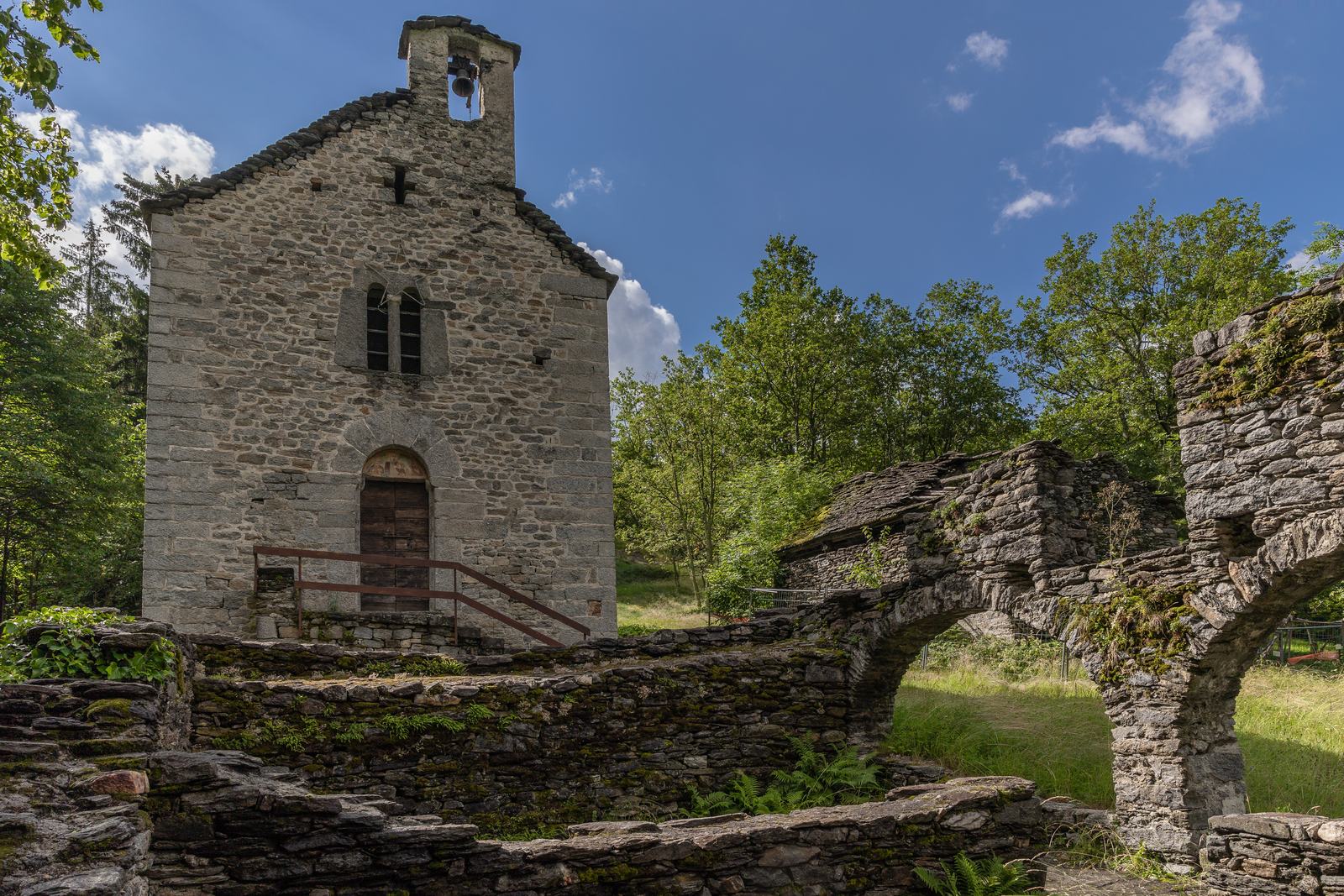 Facciata in pietra dell’oratorio di San Bernardo a Premia, con campanile e resti di muri a secco